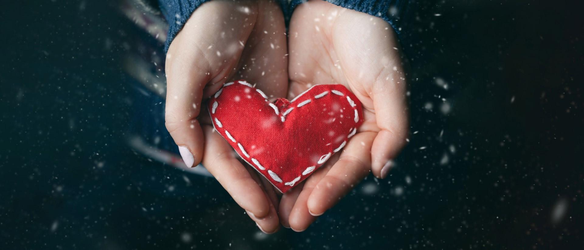 An image of two hands holding a small heart pillow.